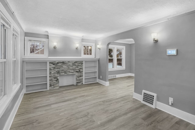 unfurnished living room featuring built in shelves, ornamental molding, a wealth of natural light, and a stone fireplace