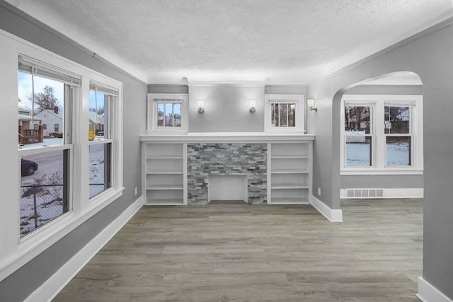 unfurnished living room featuring built in features, crown molding, a textured ceiling, and hardwood / wood-style floors