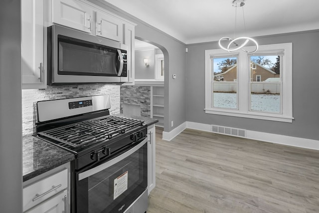 kitchen featuring hanging light fixtures, white cabinets, light wood-type flooring, dark stone countertops, and stainless steel appliances