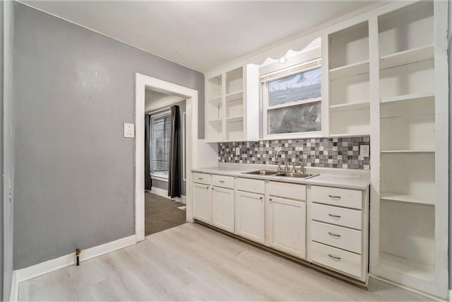 kitchen with light wood-type flooring, backsplash, white cabinetry, and sink