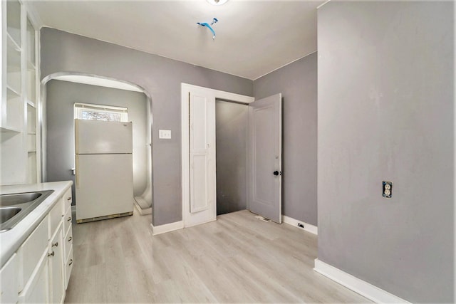 kitchen with sink, white fridge, white cabinetry, and light hardwood / wood-style flooring