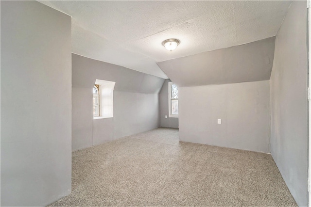 bonus room featuring a textured ceiling, light colored carpet, and lofted ceiling