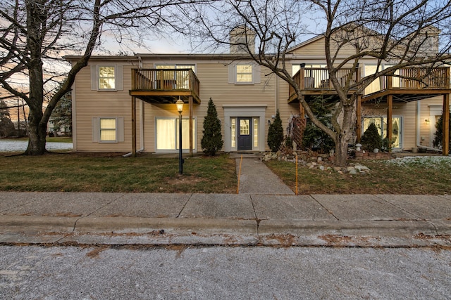 view of front facade with a balcony, a deck, and a lawn