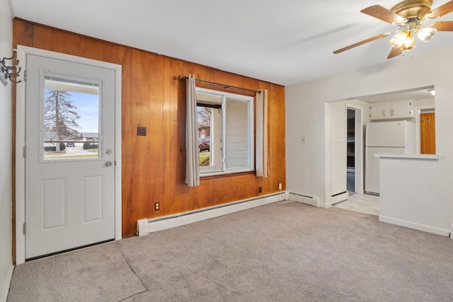 interior space featuring light colored carpet, baseboard heating, ceiling fan, and wooden walls