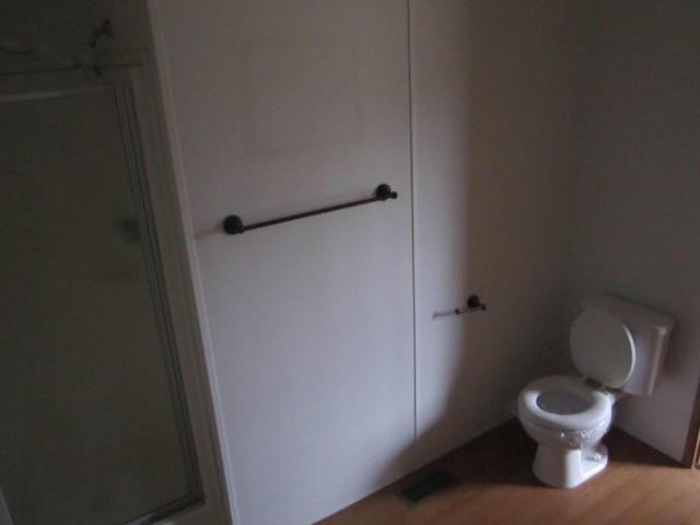 bathroom with hardwood / wood-style floors, toilet, and an enclosed shower