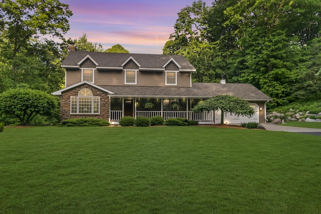 view of front of property featuring covered porch, a yard, and a garage