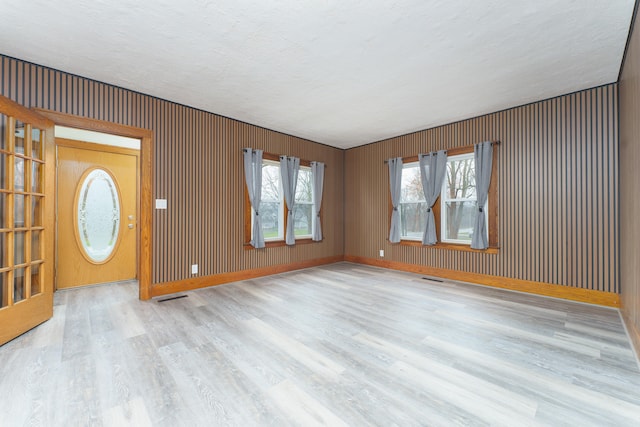 foyer entrance featuring wooden walls, light hardwood / wood-style floors, and a textured ceiling