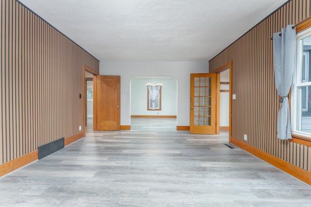 unfurnished room featuring a wealth of natural light, wooden walls, light hardwood / wood-style floors, and a textured ceiling