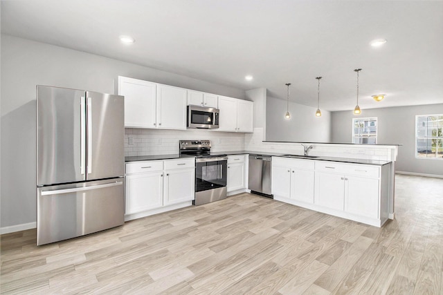kitchen featuring a sink, stainless steel appliances, light wood-style flooring, a peninsula, and white cabinetry