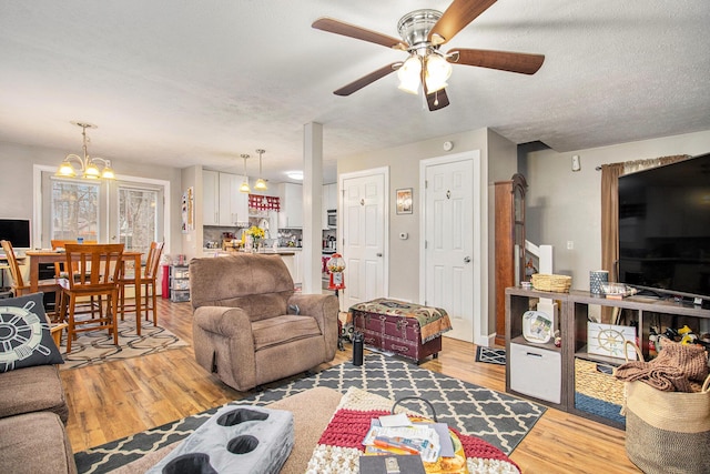 living room featuring ceiling fan with notable chandelier, wood-type flooring, and a textured ceiling