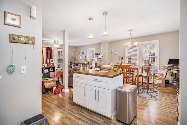 kitchen with hanging light fixtures, a kitchen island, light hardwood / wood-style flooring, butcher block countertops, and white cabinets