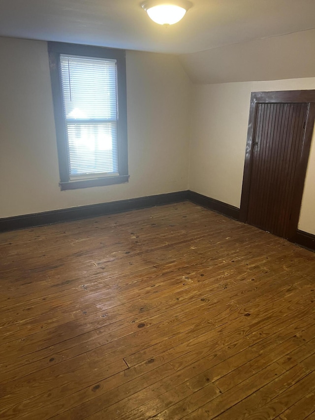 empty room with lofted ceiling, baseboards, and dark wood finished floors