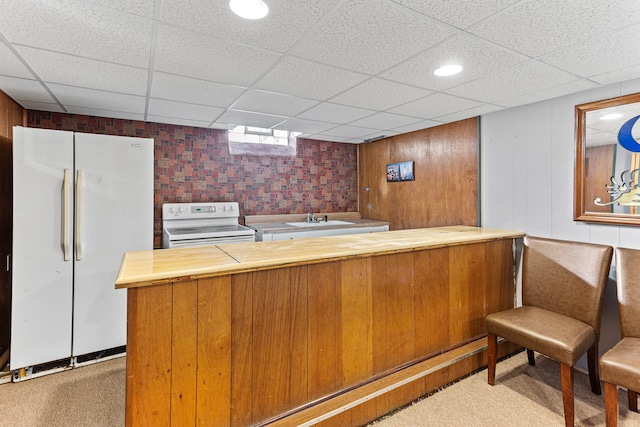 kitchen with kitchen peninsula, carpet floors, wooden walls, and white appliances