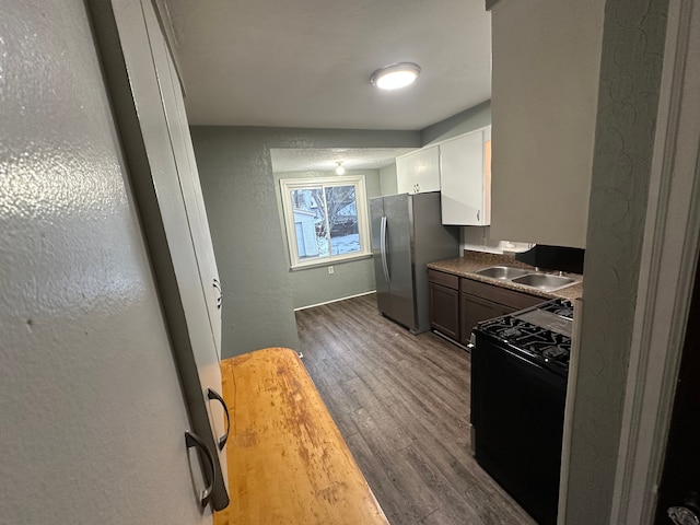 kitchen featuring stainless steel refrigerator, sink, dark wood-type flooring, black range, and white cabinets