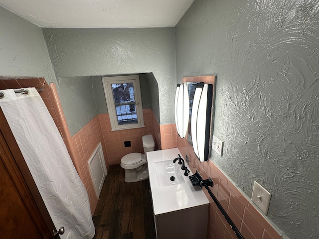 bathroom featuring wood-type flooring, vanity, toilet, and tile walls