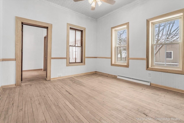 empty room with light hardwood / wood-style floors, crown molding, a wealth of natural light, and a baseboard heating unit