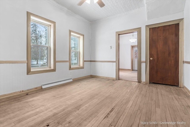 spare room with a baseboard radiator, ceiling fan, light hardwood / wood-style floors, and wood walls