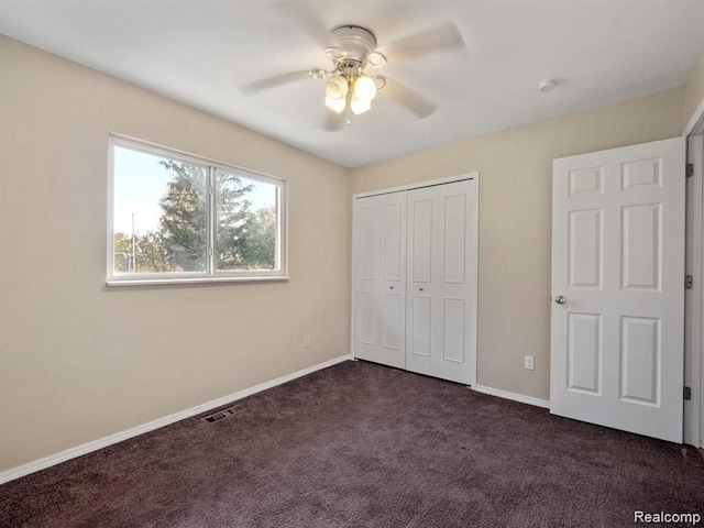 unfurnished bedroom with ceiling fan, a closet, and dark colored carpet