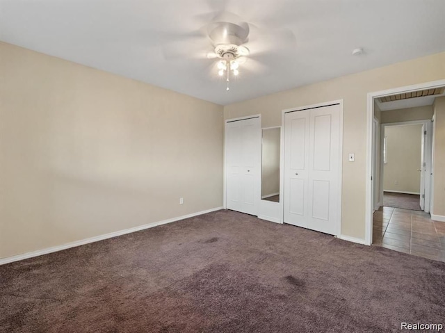 unfurnished bedroom featuring ceiling fan, dark carpet, and two closets