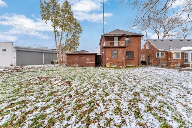 snow covered rear of property with a balcony and an outbuilding