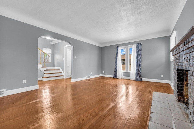 unfurnished living room with light hardwood / wood-style floors, a textured ceiling, a wealth of natural light, and a brick fireplace