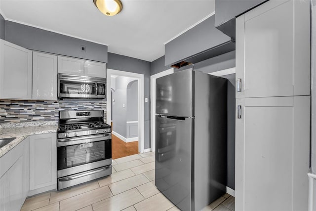 kitchen featuring white cabinetry, stainless steel appliances, tasteful backsplash, light stone counters, and light hardwood / wood-style floors