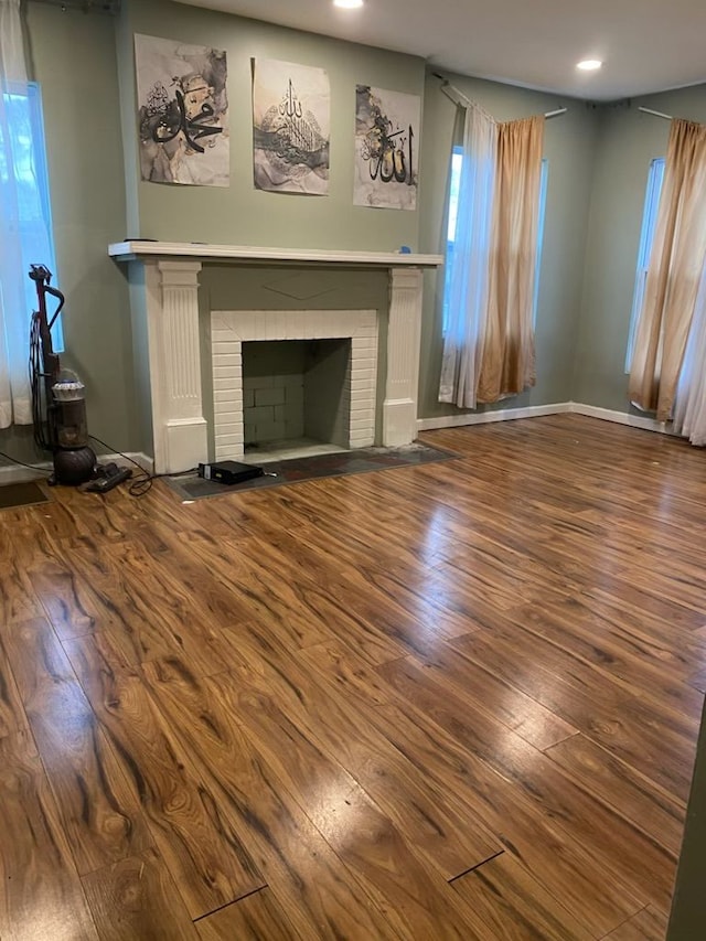 unfurnished living room featuring hardwood / wood-style flooring and a brick fireplace