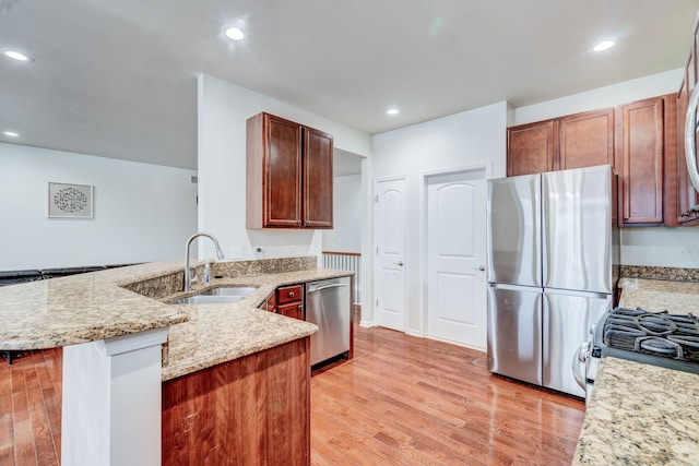 kitchen with kitchen peninsula, light wood-type flooring, light stone counters, stainless steel appliances, and sink