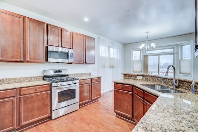 kitchen featuring light stone countertops, sink, stainless steel appliances, an inviting chandelier, and pendant lighting