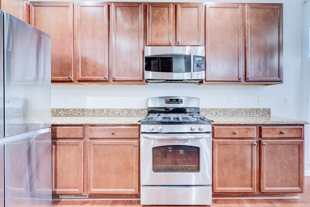 kitchen with light stone counters, light wood-type flooring, and appliances with stainless steel finishes