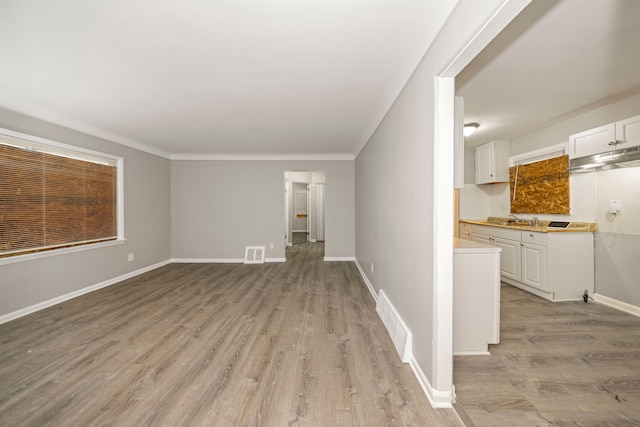 unfurnished living room featuring ornamental molding, sink, and light hardwood / wood-style flooring