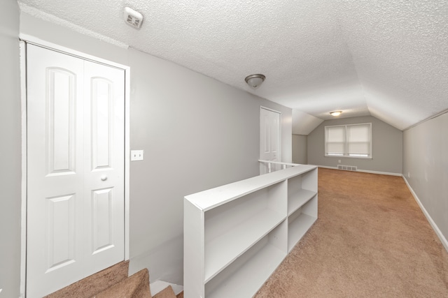 corridor featuring light colored carpet, lofted ceiling, and a textured ceiling