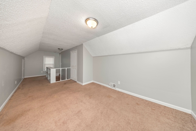 additional living space featuring lofted ceiling, light colored carpet, and a textured ceiling