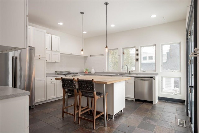 kitchen featuring white cabinets, decorative light fixtures, a center island, and stainless steel appliances