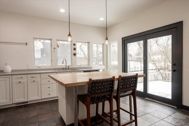 kitchen featuring wooden counters, a kitchen island, sink, white cabinetry, and hanging light fixtures