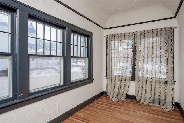 unfurnished room featuring hardwood / wood-style flooring, a textured ceiling, and vaulted ceiling