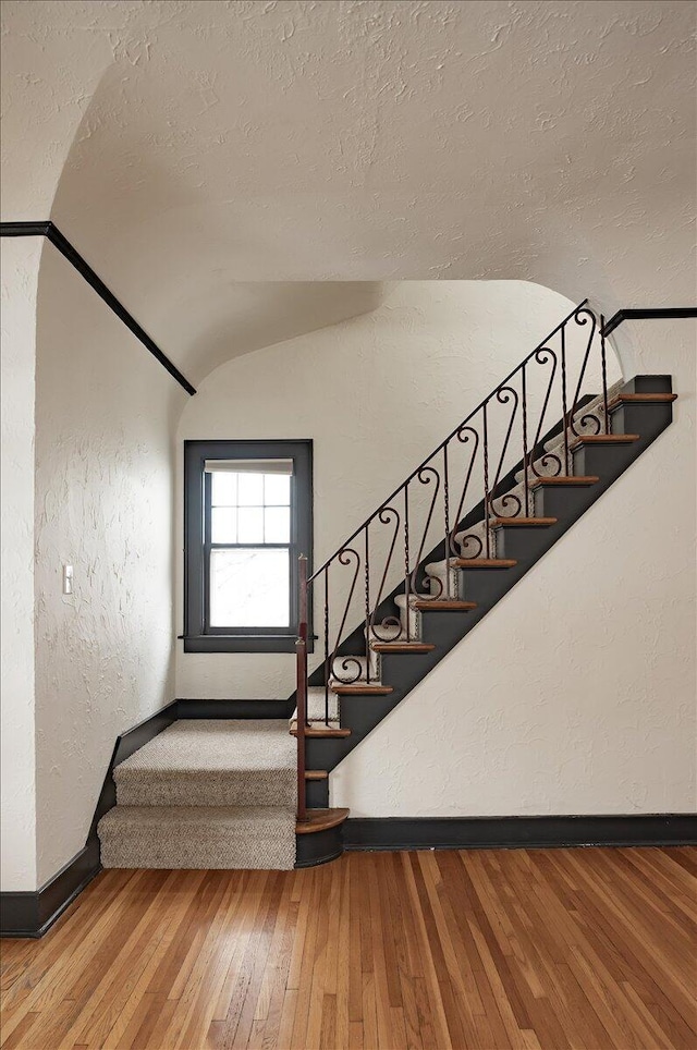 staircase featuring a textured ceiling, vaulted ceiling, and hardwood / wood-style flooring