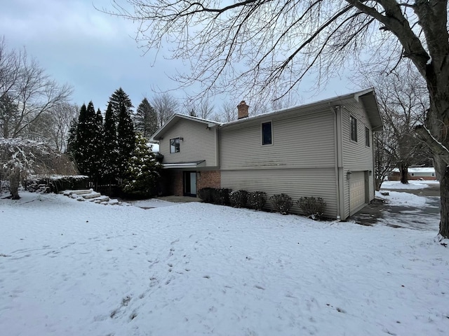 snow covered back of property featuring a garage