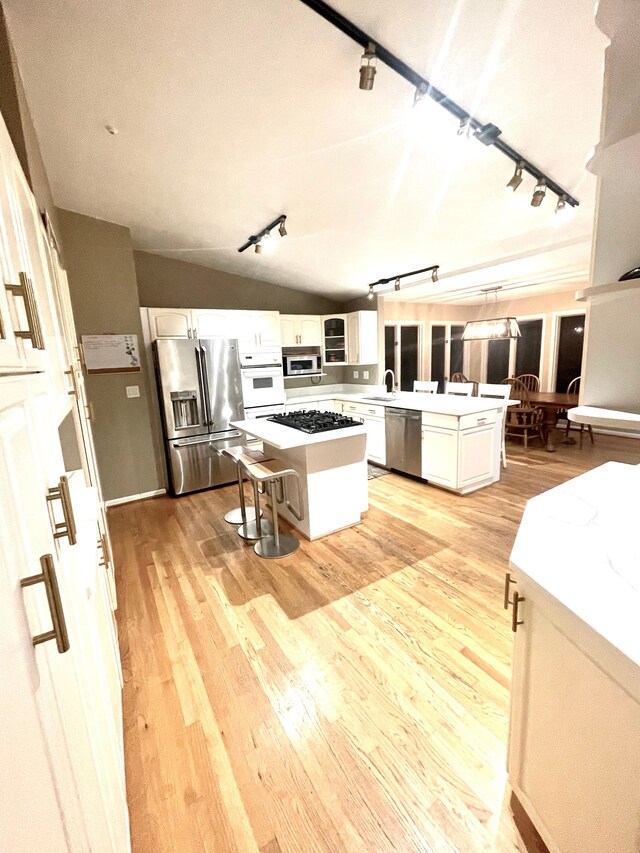 kitchen with a center island, lofted ceiling, light wood-type flooring, appliances with stainless steel finishes, and white cabinetry