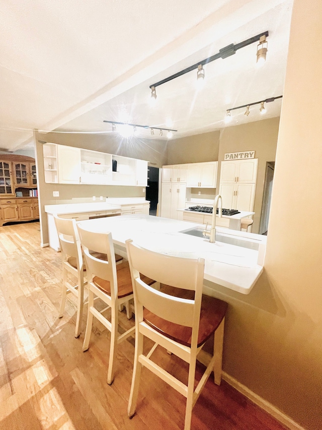 kitchen featuring white cabinets, a kitchen breakfast bar, light wood-type flooring, and track lighting