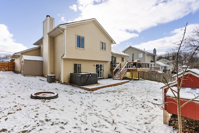 snow covered property with a wooden deck, a shed, central AC, an outdoor fire pit, and a hot tub