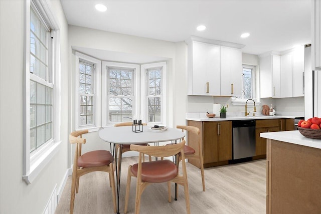 kitchen featuring light hardwood / wood-style flooring, white cabinets, stainless steel dishwasher, and sink