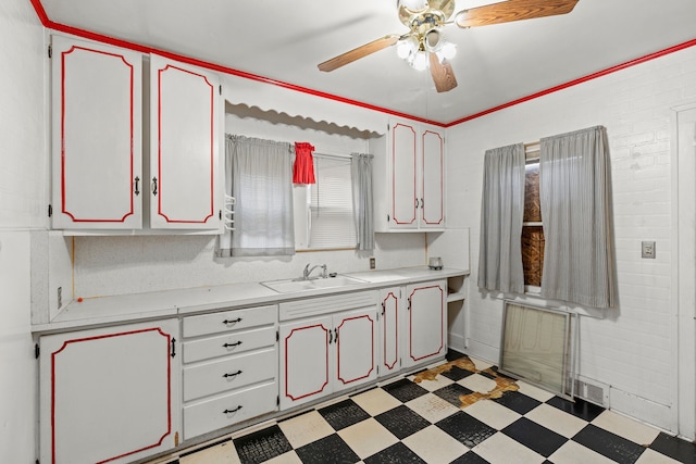 kitchen featuring ceiling fan, sink, white cabinets, and brick wall