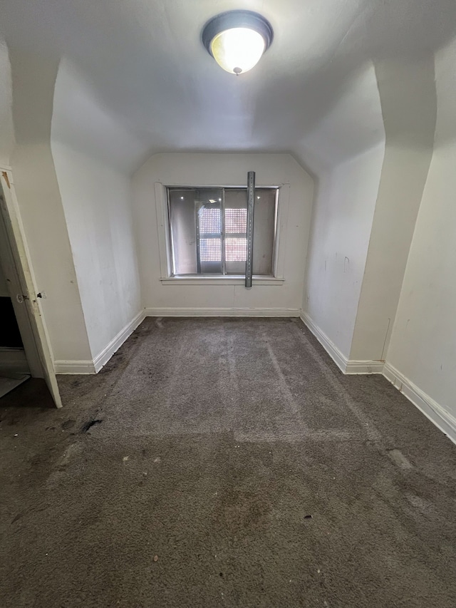 additional living space featuring dark colored carpet and lofted ceiling