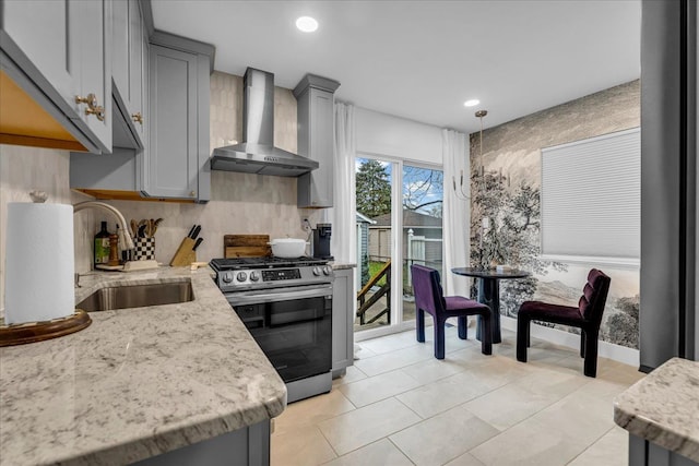 kitchen with stainless steel gas range oven, sink, gray cabinets, and wall chimney range hood