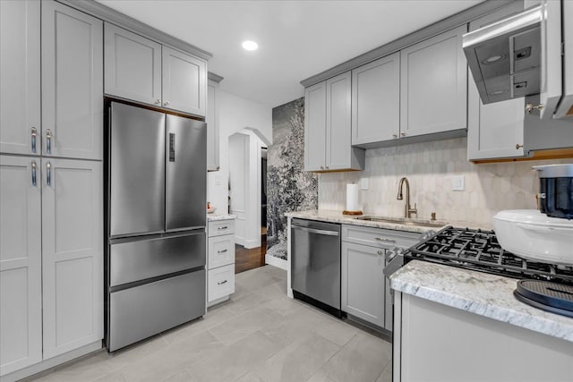 kitchen with gray cabinetry, sink, light stone counters, backsplash, and appliances with stainless steel finishes