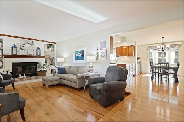 living room with light hardwood / wood-style floors, a brick fireplace, and a notable chandelier