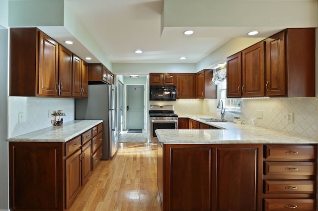 kitchen featuring appliances with stainless steel finishes, sink, light stone counters, kitchen peninsula, and light wood-type flooring