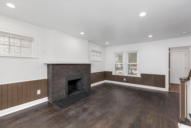 unfurnished living room with a fireplace, wood walls, and dark wood-type flooring