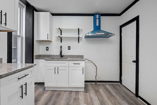 kitchen featuring hardwood / wood-style floors, wall chimney range hood, sink, light stone counters, and white cabinetry